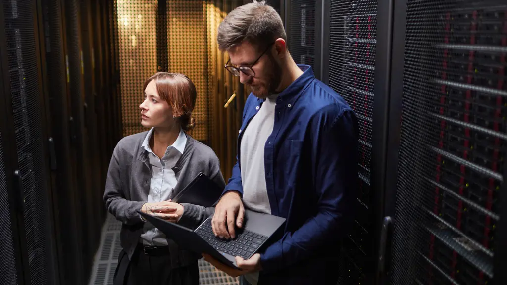 Two engineers in a server-room aisle looking at a laptop