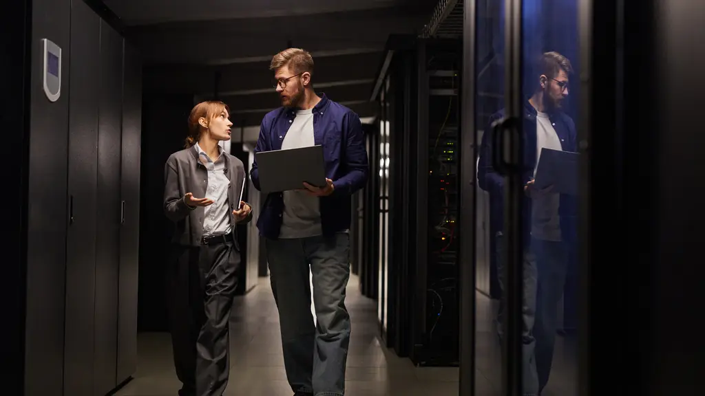 Two engineers walking down a dark server-room aisle